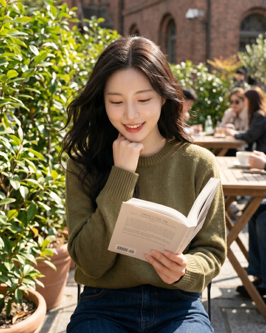 Woman in a green sweater smiling while reading a book at an outdoor café