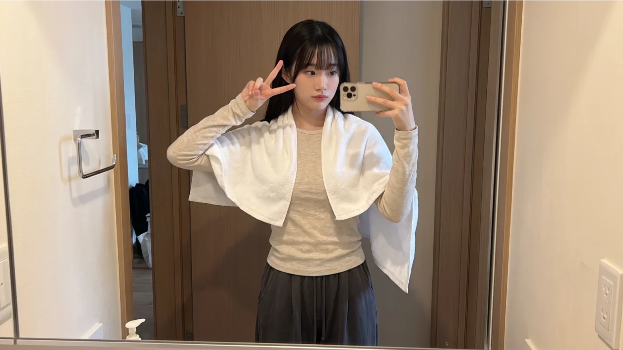 Young woman with natural straight black hair taking a mirror selfie with a white towel draped over her shoulders after a hair care routine